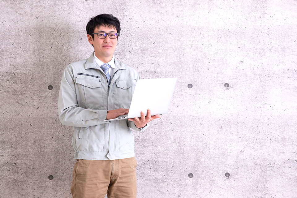 ノートパソコンを持つ作業服の男性