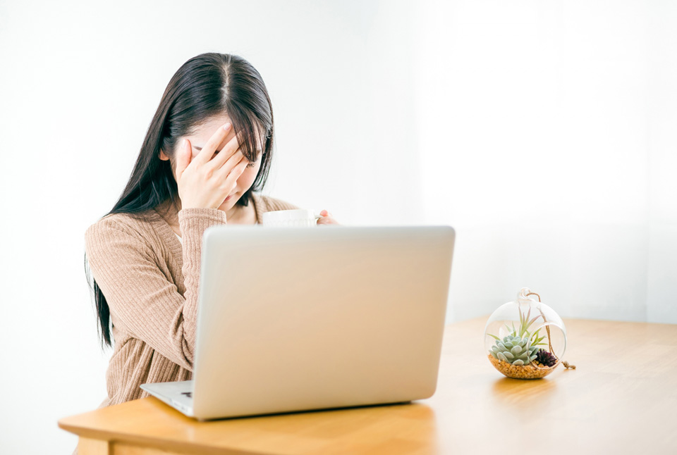 ノートパソコンの前で頭を抱える女性