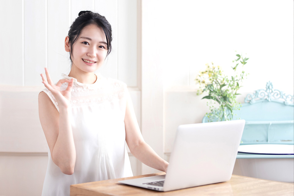 ノートパソコンの前でOKサインを出す女性