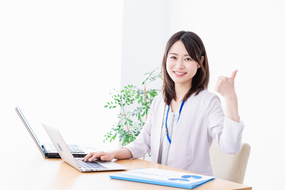 ノートパソコンの前でグッドポーズをする女性